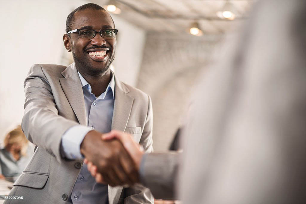Happy African American businessman shaking hands with his unrecognizable colleague.